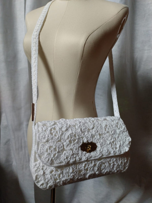 Scopri Fiorella la Borsa, realizzata a mano in cotone bianco all'uncinetto. Design elegante con fiori, chiusura in metallo e tracolla in cotone. Perfetta per ogni occasione!